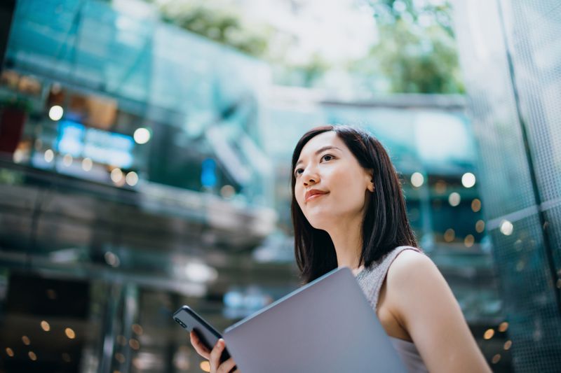 Young, successful businesswoman carrying a smartphone and a laptop. 