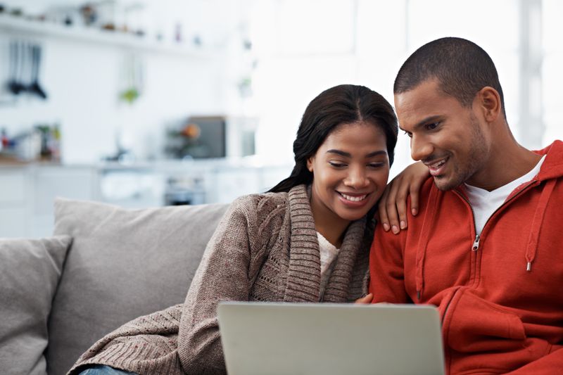 Young couple sitting on their sofa and looking happily at mortgage rates on a laptop