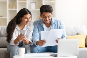 Young couple sitting on their sofa and looking at mortgage documents and rates on their laptop