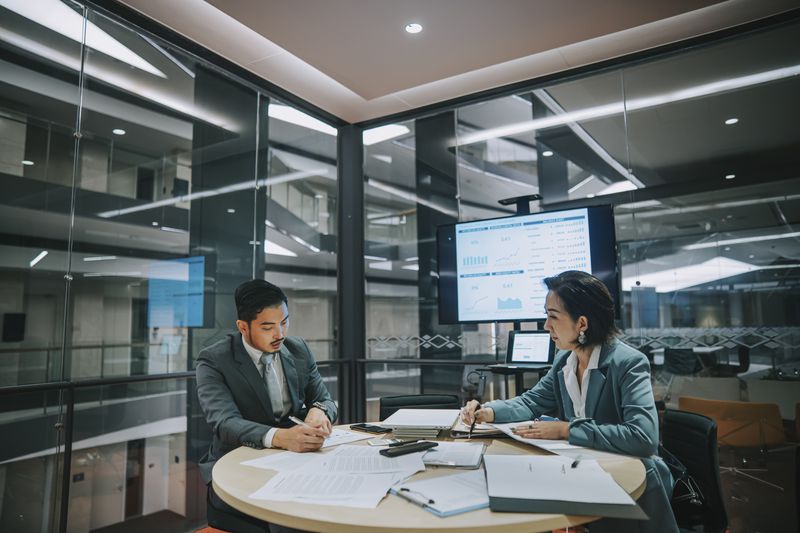 Two business executives meet in the office of an acquired firm to complete SEC documents to suspend reporting requirements.