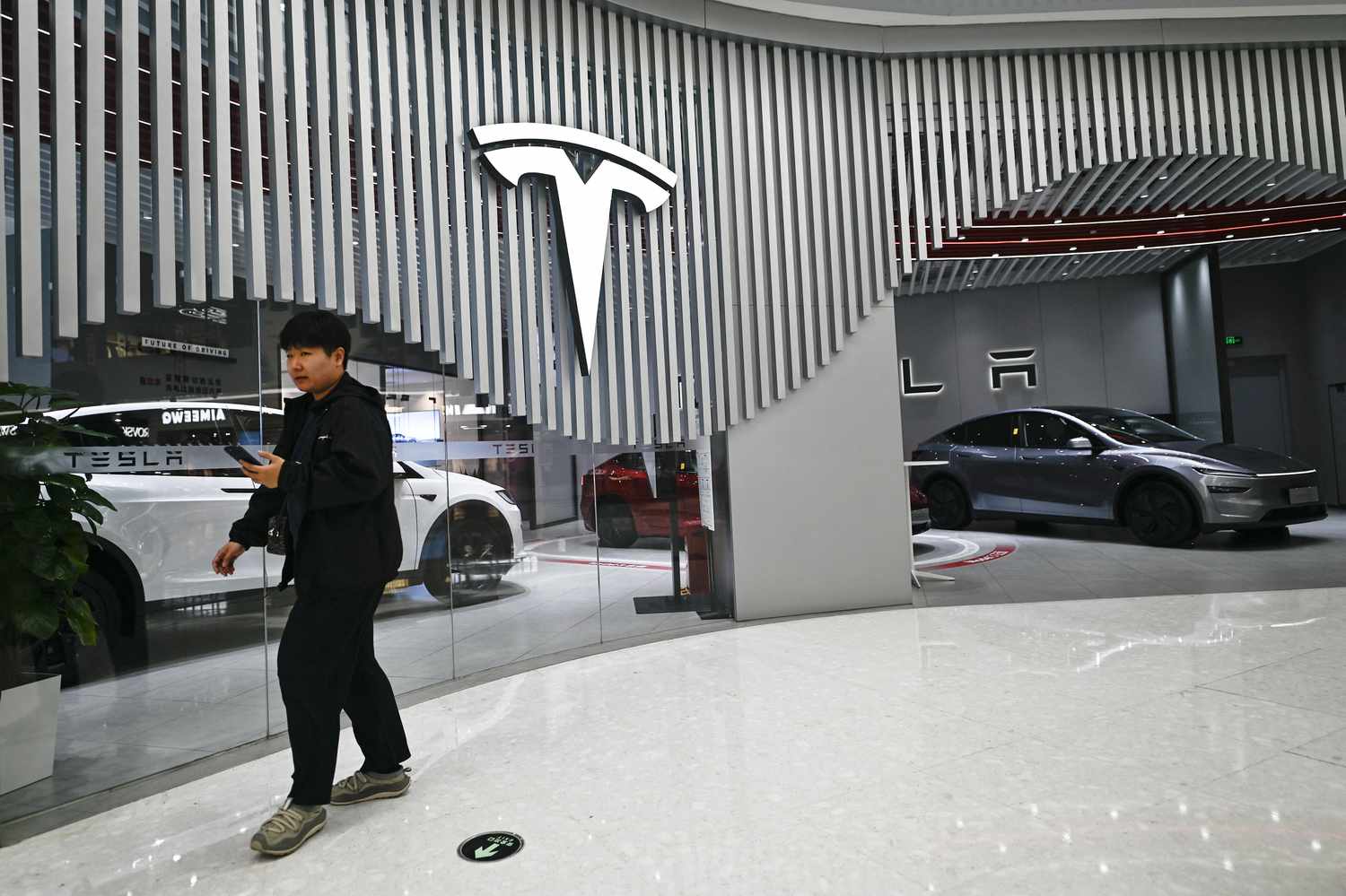 A person walks outside a Tesla showroom, with the company's logo next to the entrance.