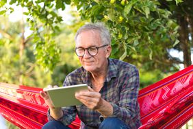 Retiree in hammock looking at a tablet
