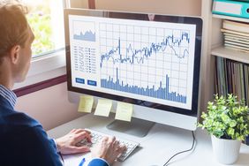 Man at desk looking at candlestick chart on monitor