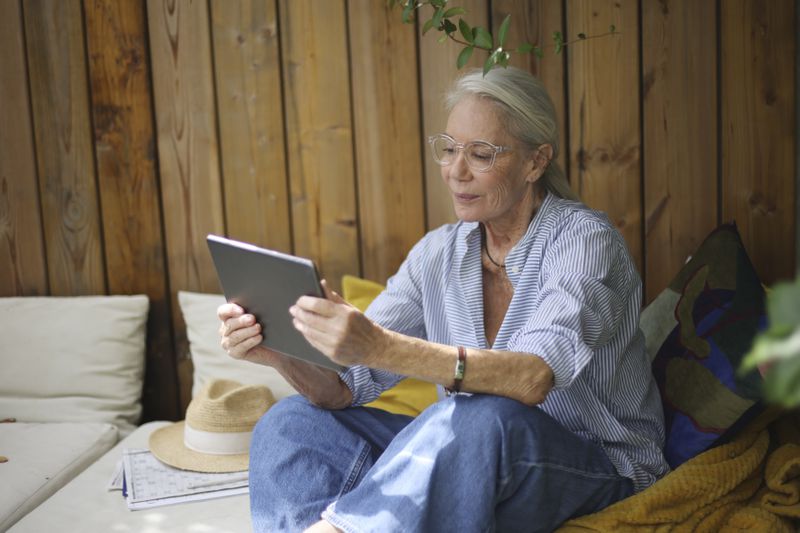 An older woman looking at a tablet on her balcony