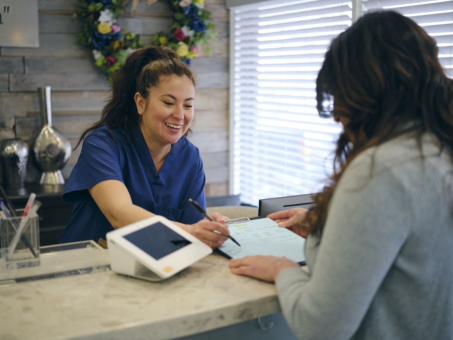 Woman at the front desk in a doctor's office showing paperwork to a patient