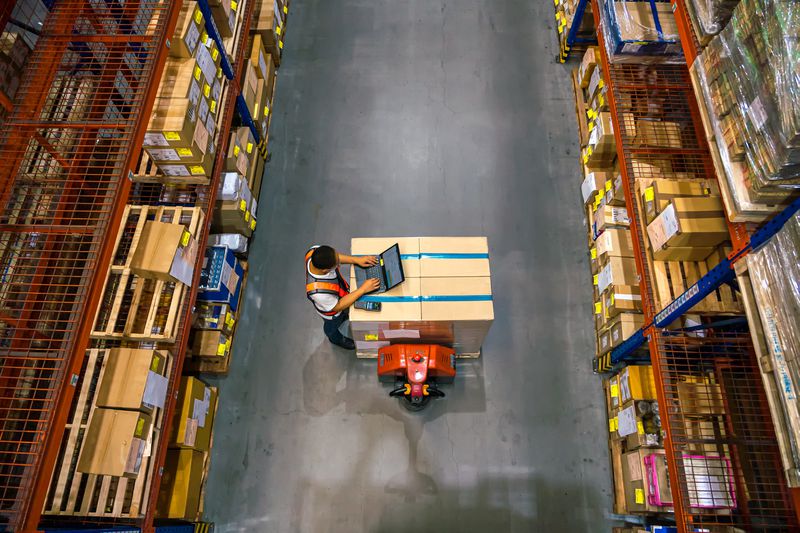 Top view of warehouse worker using laptop to check location of goods