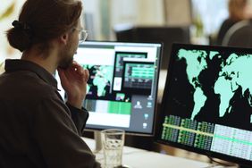 Young man sitting before a computer monitor showing a map of the world