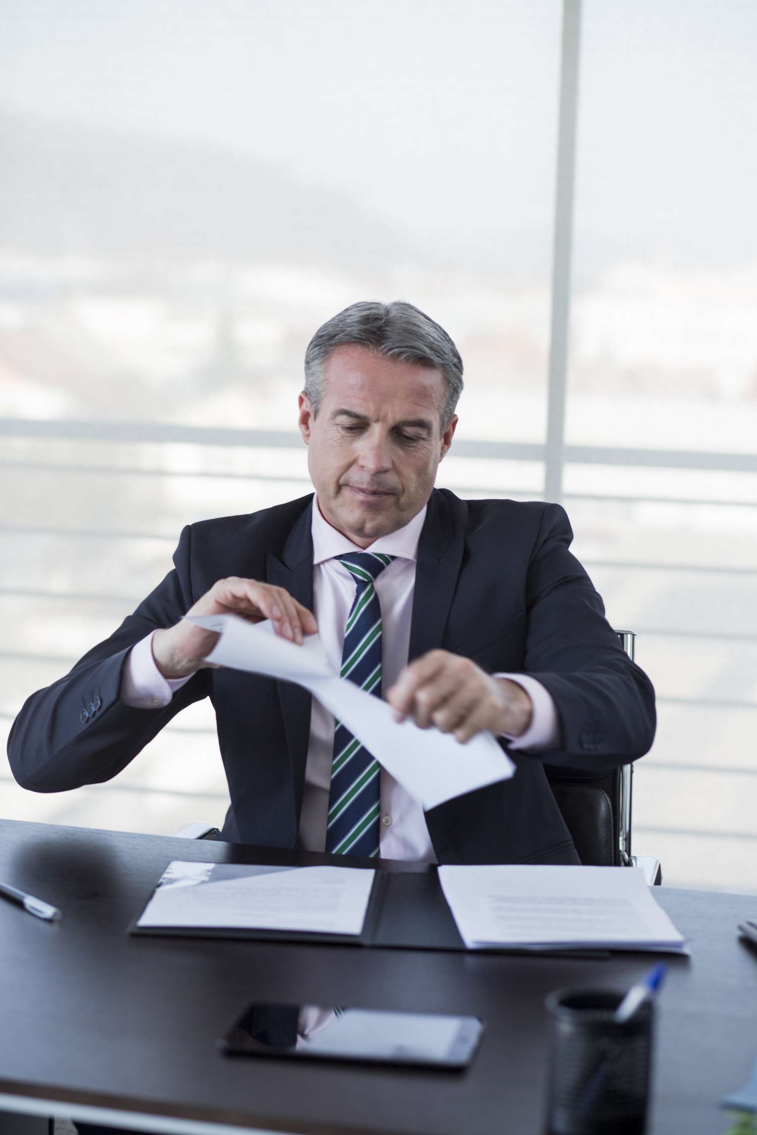 Senior banker sitting at his desk opening a deceased alert in his office