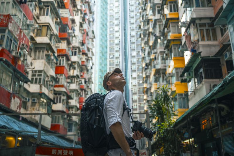 A person with a backpack and camera looks up between tall residential buildings