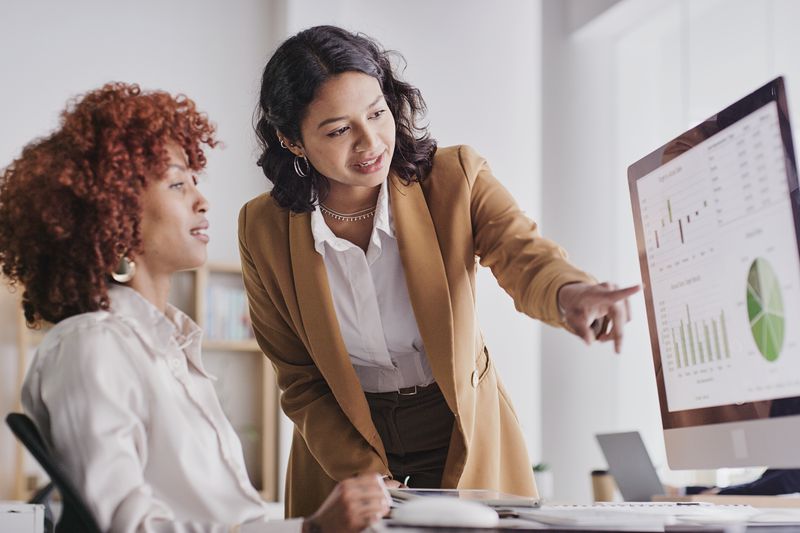 Two women looking at graphs and other data on a computer