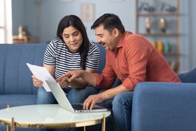 Couple in their 30s sitting in their living room and looking at mortgage documents and a laptop