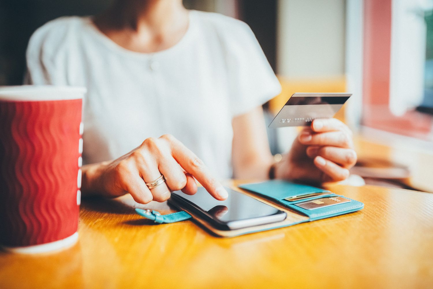 A person sitting by the window in a cafe using a credit card to do balance transfer in order to pay down an old debt.