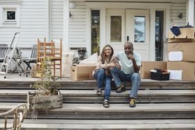 Man and woman sitting on steps outside of a house with moving boxes next to them