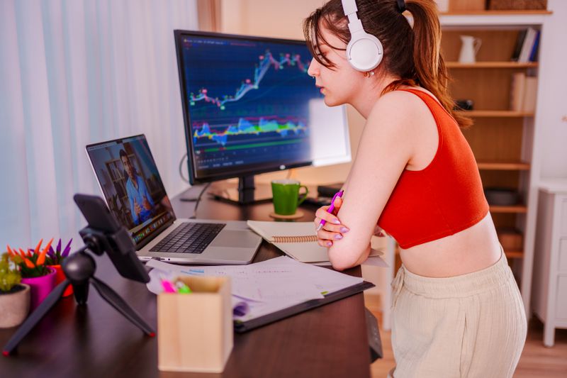 Woman standing before an open laptop. The monitor next to her displays a chart.