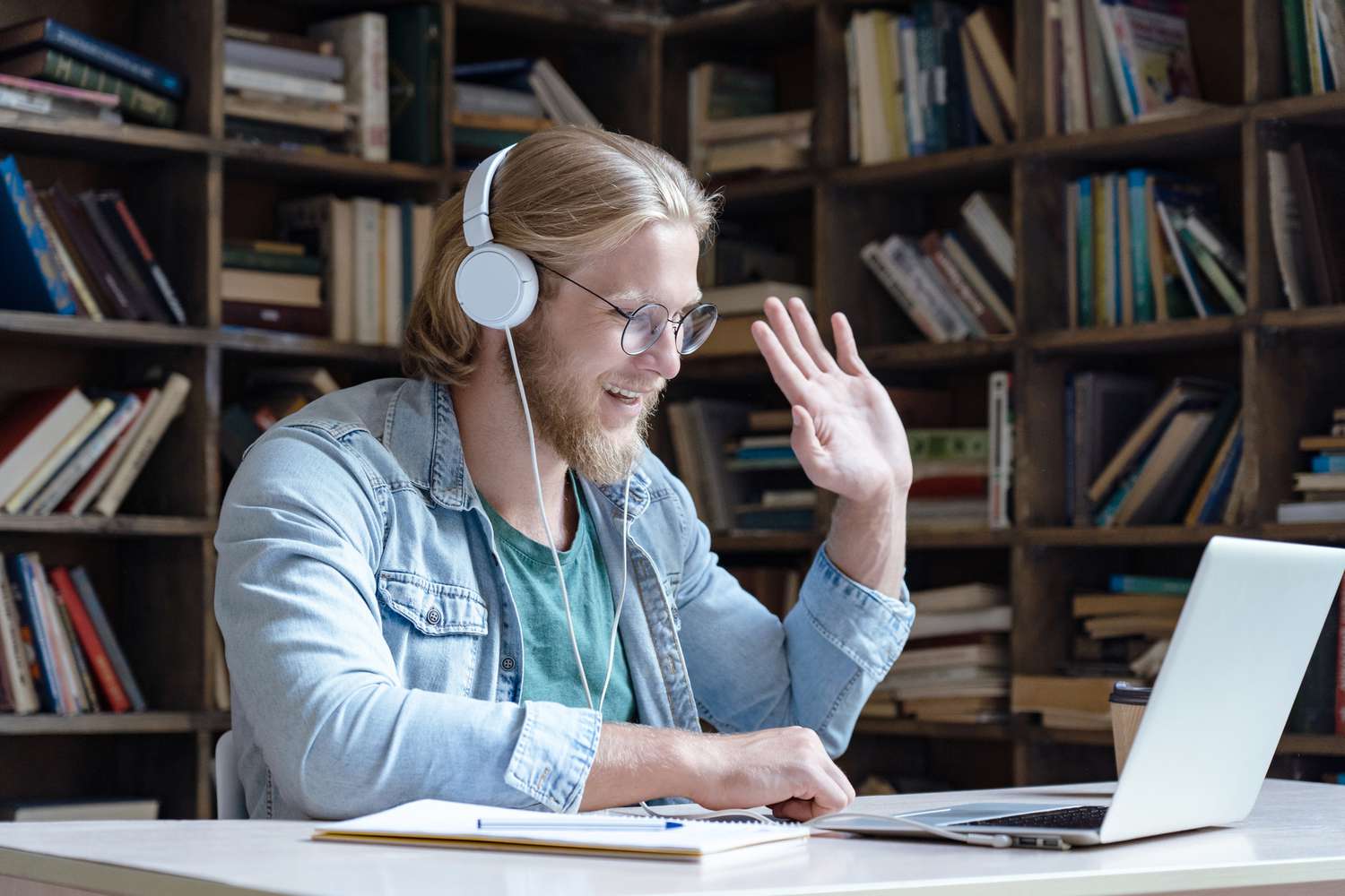 Happy student wear headphones waving hand looking at laptop computer screen video conference talking with online skype teacher communicating for distance education e learning in library