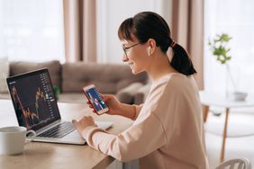 Female trader looking at charts on laptop and mobile device