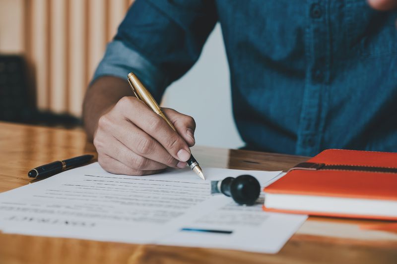 Close up of customer signing contract with fancy, heavy pen while sitting at desk