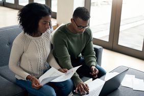 Young couple sitting on their sofa and looking at mortgage documents and a laptop