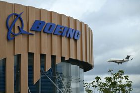 The blue Boeing logo on the side of an office building, with a plane flying by in the background