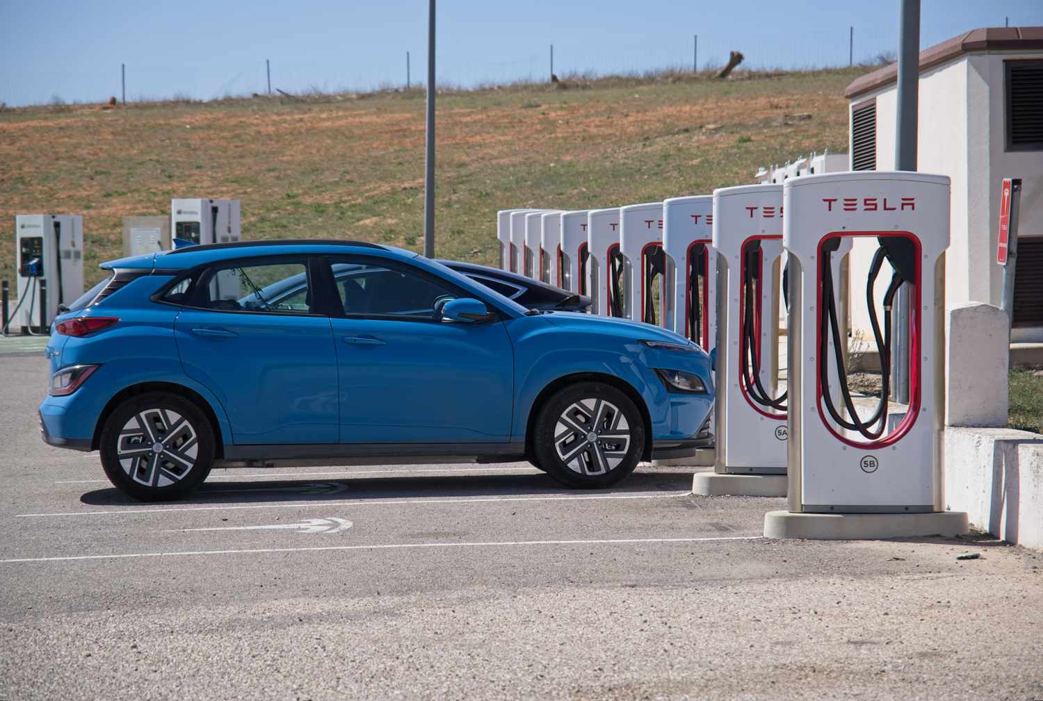 A static shot of a solid black Tesla Model 3 dual motor charging at the Atalaya del Canavate Supercharger in a sunny spring day.