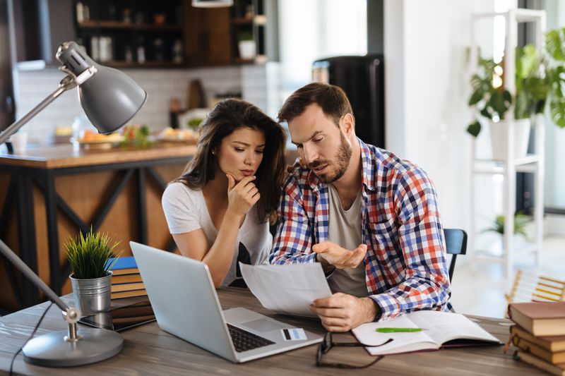 Frustrated couple checking bills at home using laptop