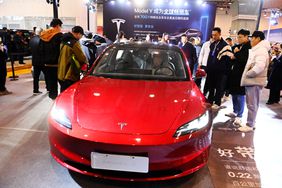 A group of people stand around a red Tesla vehicle on the floor of a car show in China.