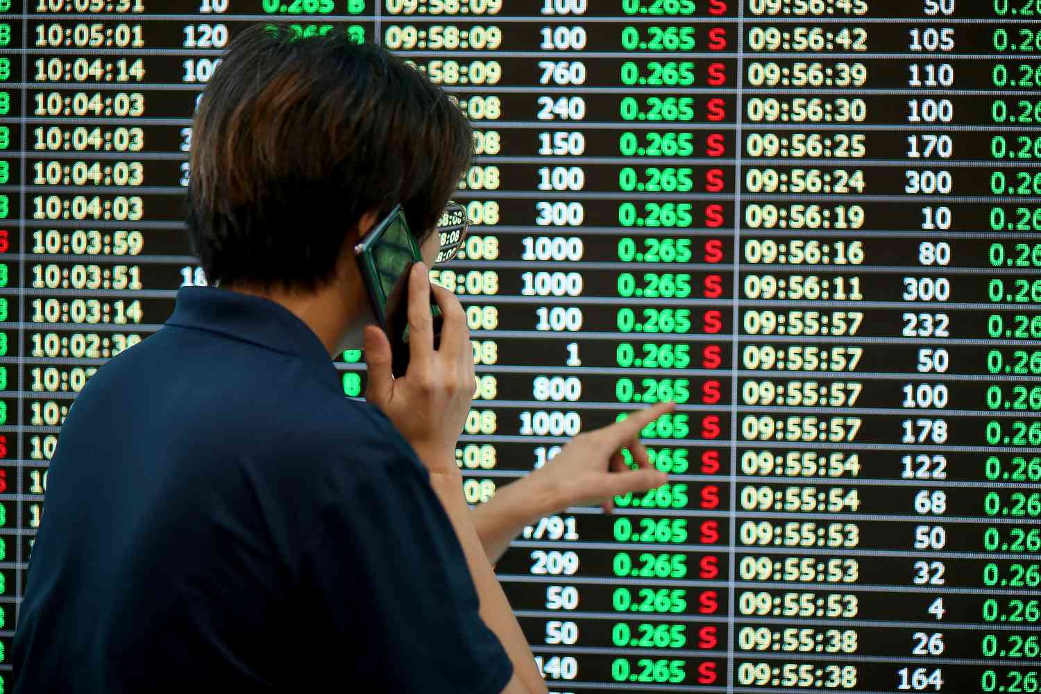 Stock trader talking on cellphone while monitoring stock prices.