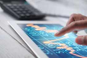 A person using a tablet with a linear graph display, a calculator in the background