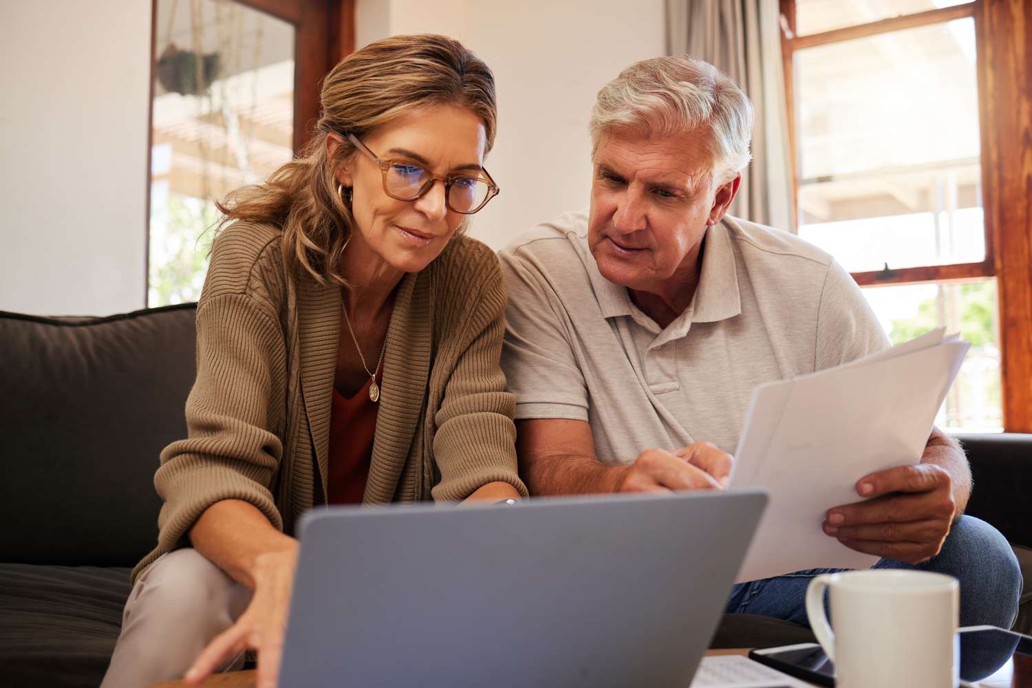 Older couple sitting on their sofa and looking together at documents and a laptop