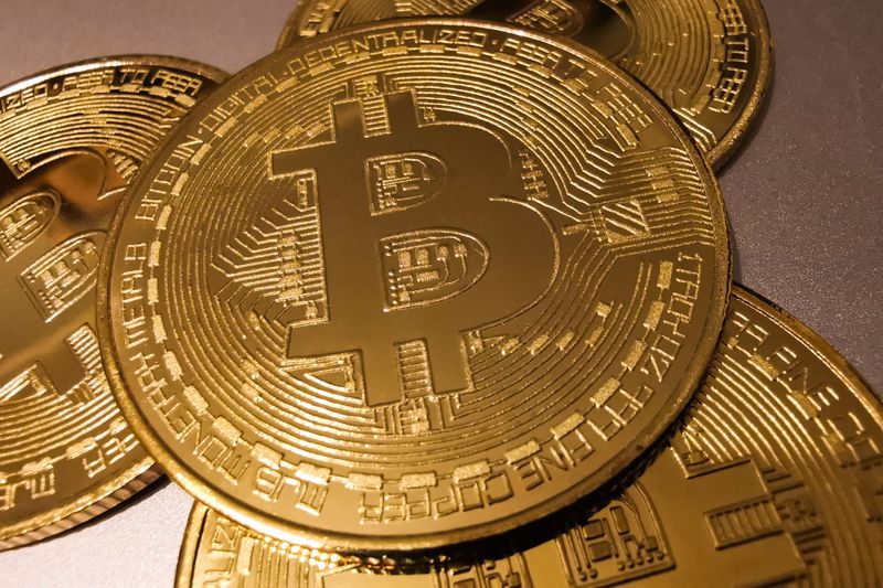 A stack of gold coins with the Bitcoin "B" symbol sit on a table.