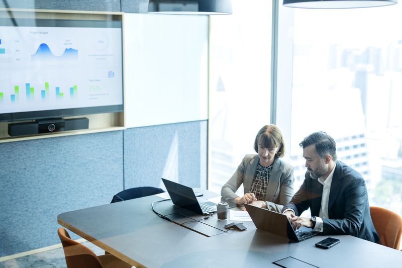 People working in a conference room with charts on a wall screen