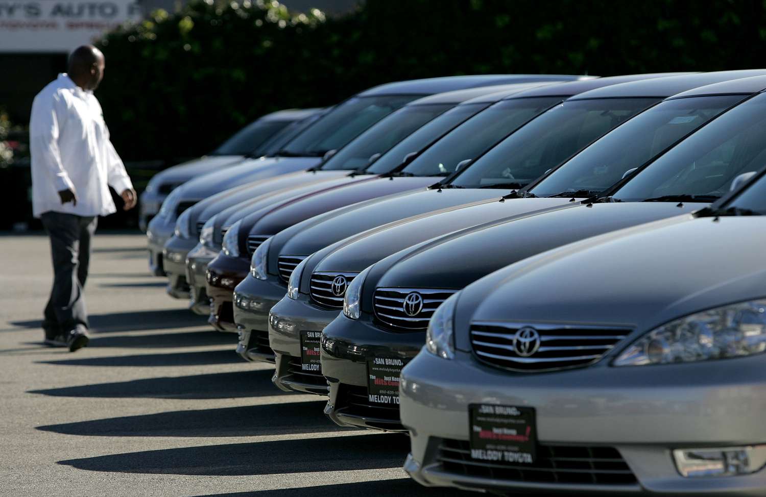 A man walks near a row of cars for sale.