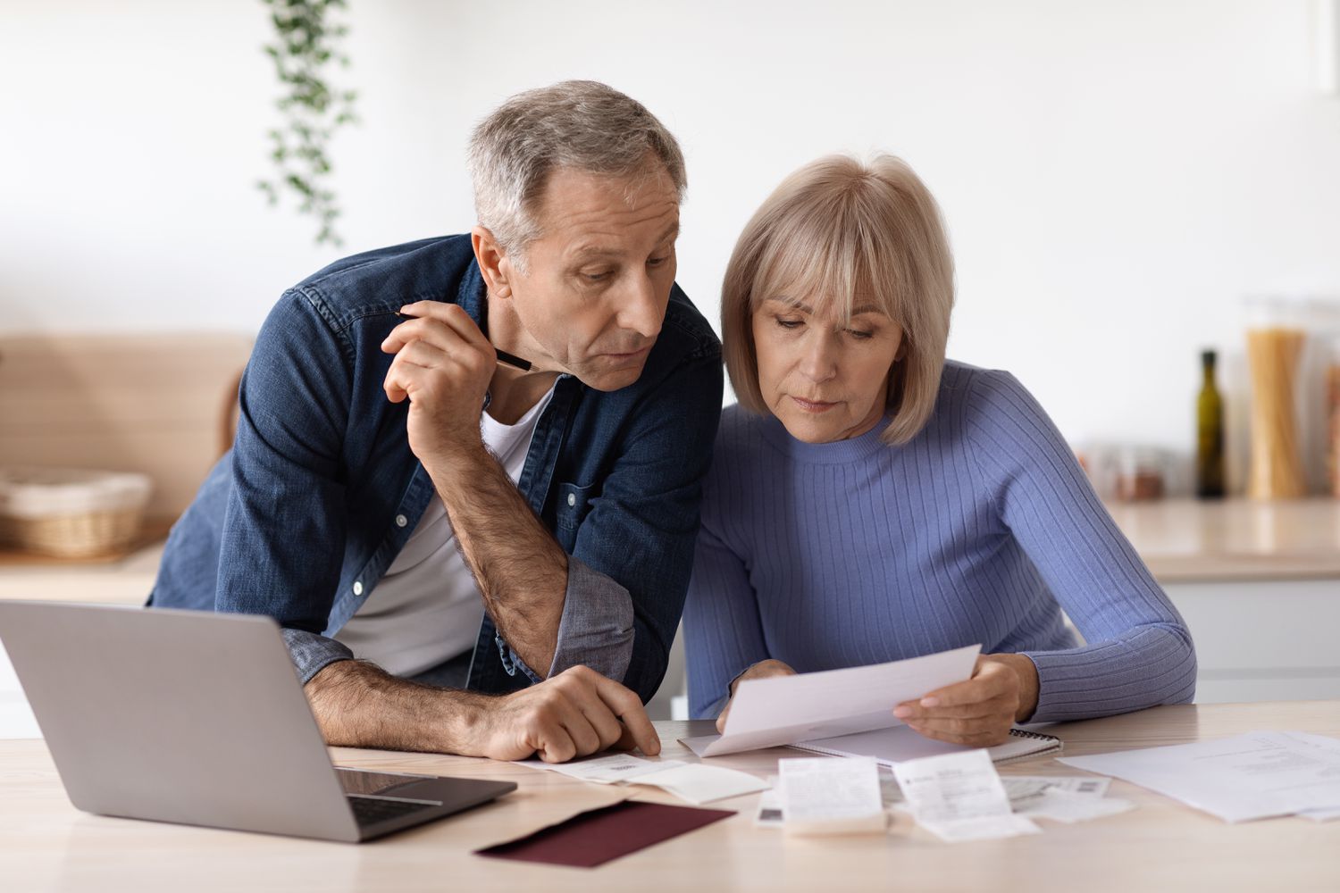 Older couple sitting at their kitchen counter and looking at mortgage documents and a laptop