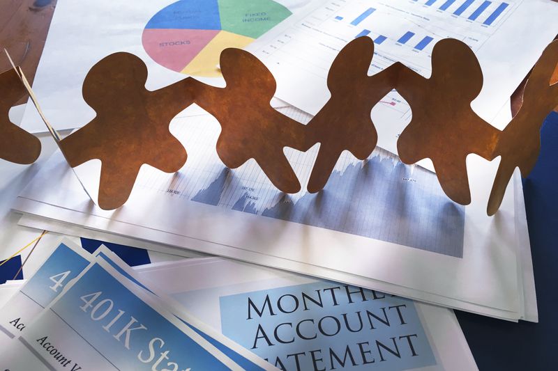 A paper doll chain rests on top of a 401K statement and financial charts representing ethical investing concept