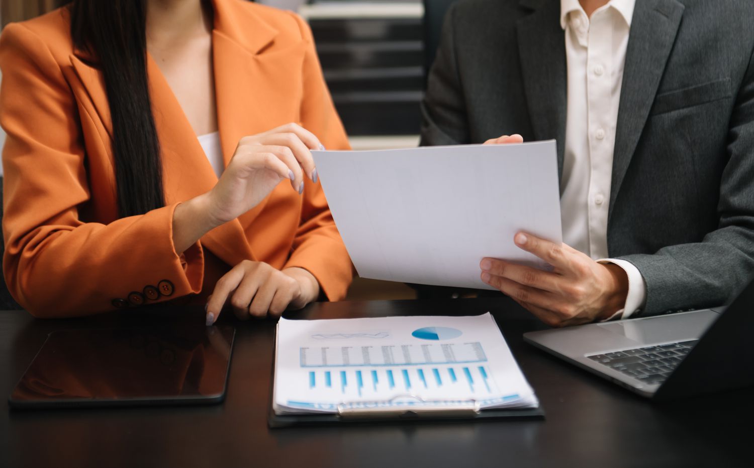 Cropped shot showing the torsos of two business people sitting at a desk discussing a document they hold before them.