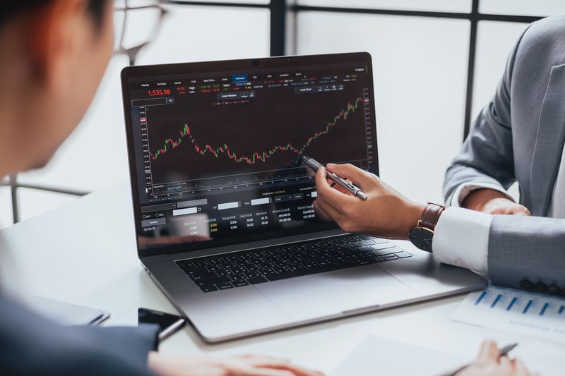 Man in business suit pointing with a pen to a computer with stock trading information