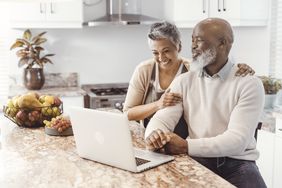 A couple smiling together as they use a laptop in a kitchen