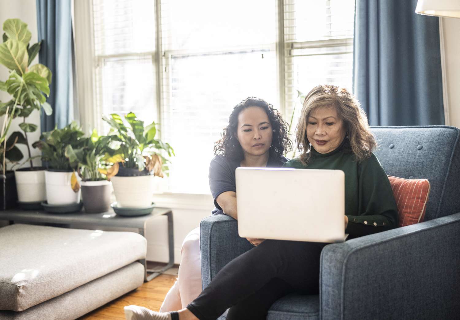An older woman and her adult daughter look at a laptop together in a living room