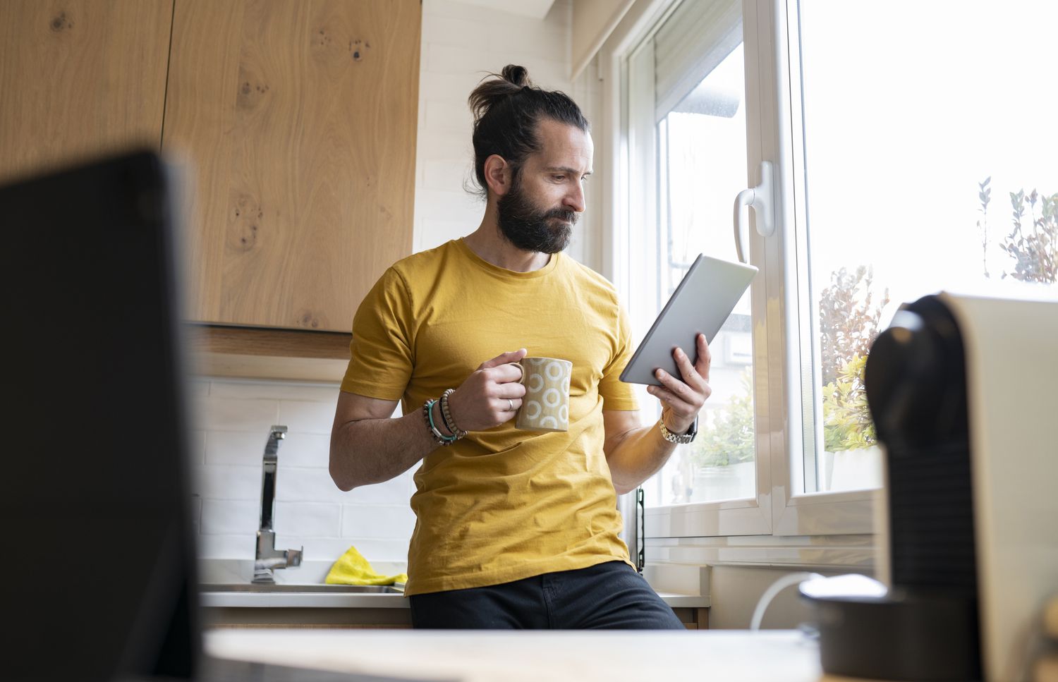 Person holding coffee mug looks at digital tablet in kitchen