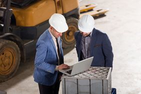 Hig angle view of two men in hard hats discussing something on a laptop.