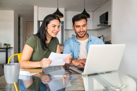 Young couple sitting in their kitchen and looking at mortgage documents and a laptop