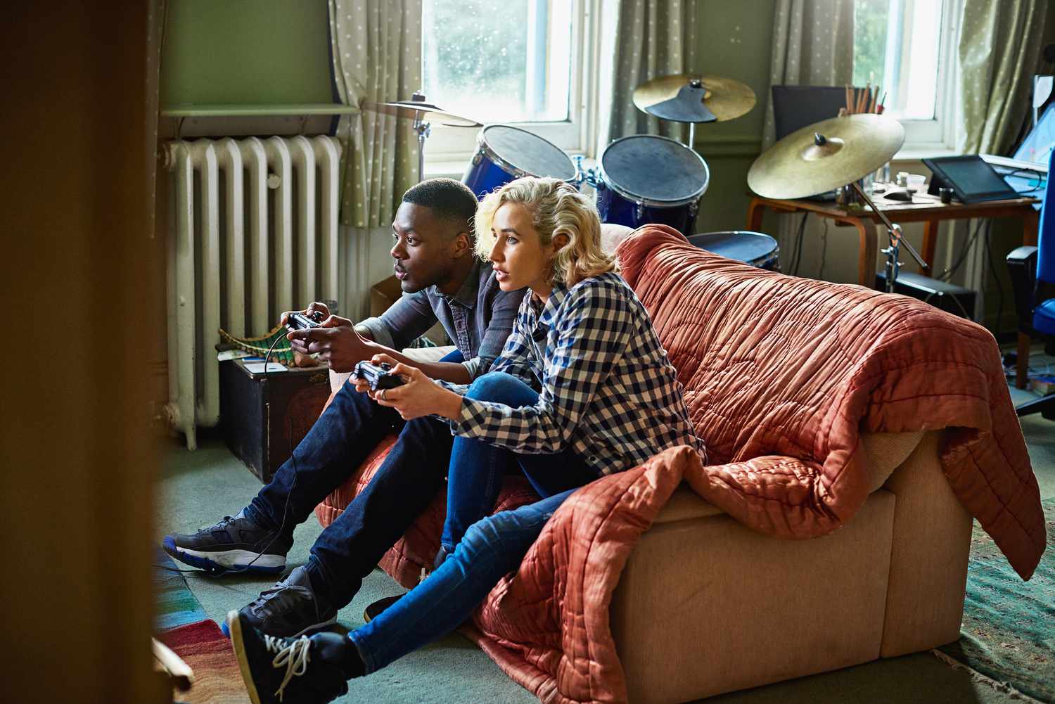 Two young adults playing console video games sitting on a couch in a small apartment.