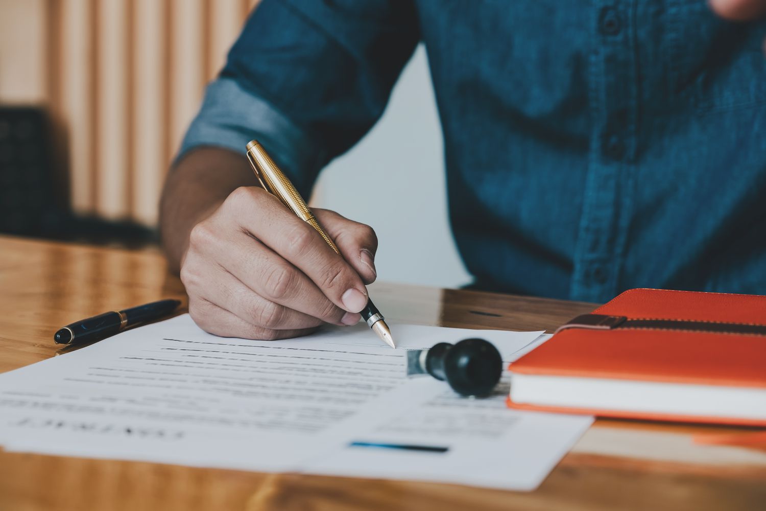 Close up of customer signing contract with fancy, heavy pen while sitting at desk