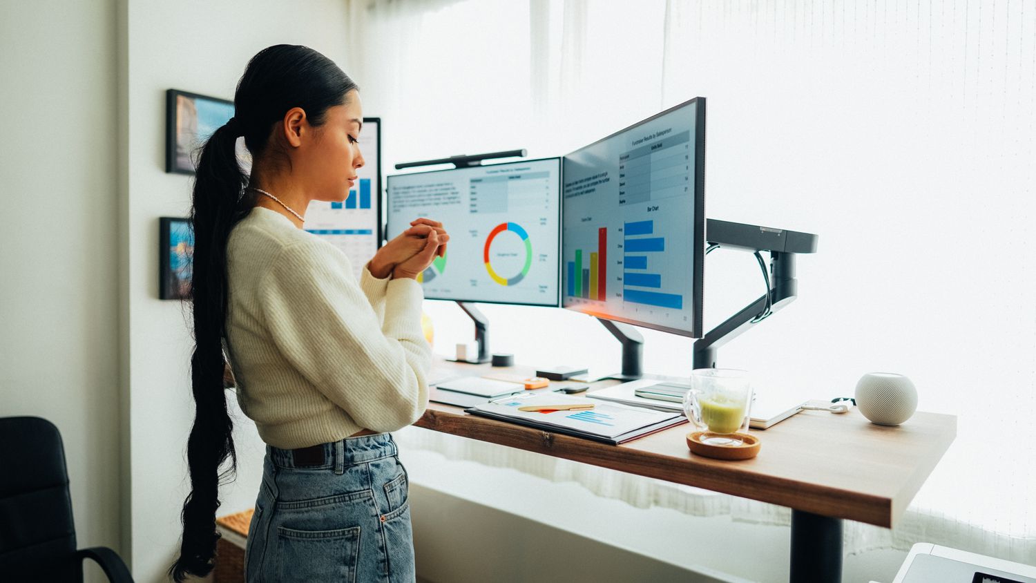 Woman standing win front of a desk with multiple monitors showing charts and other data.
