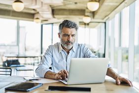 Mature man with beard looking intently at his laptop