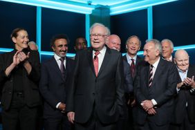Warren Buffett in a suit in front of other businesspeople on a stage.