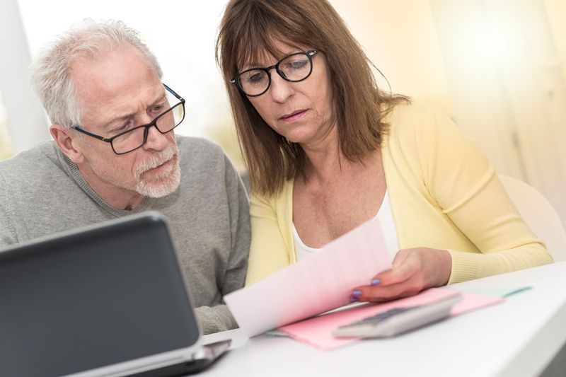 Couple in their 50s or 60s sitting at home and looking at mortgage documents and a laptop