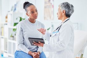Female doctor talks to young woman patient while holding a tablet computer 