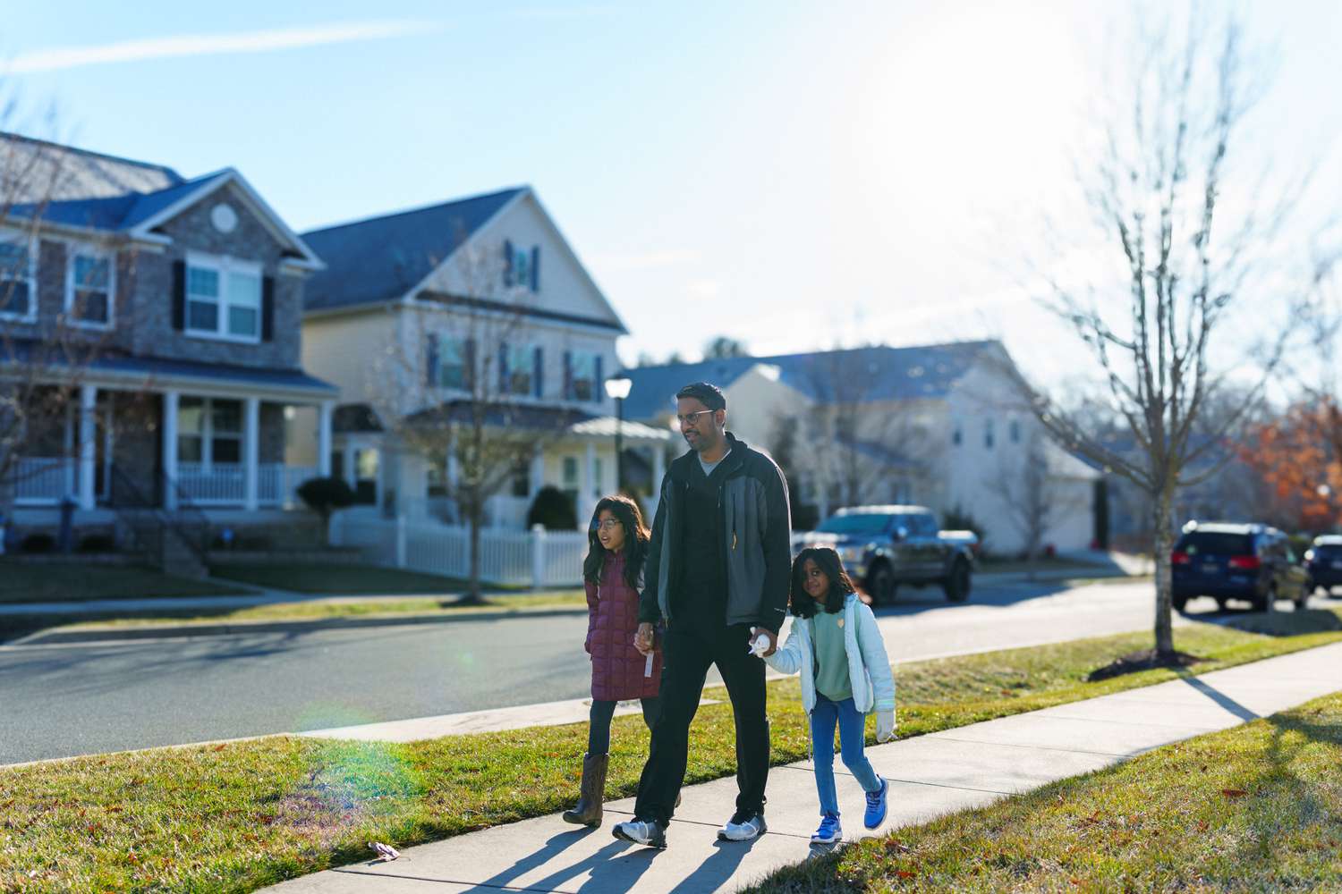 A father walks down the street with his two daughters holding hands