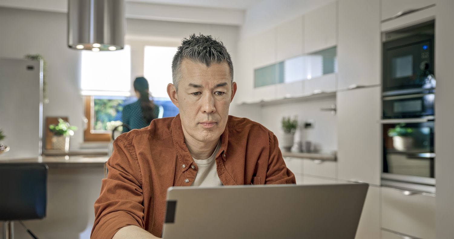 Mature man working on laptop while sitting in kitchen.